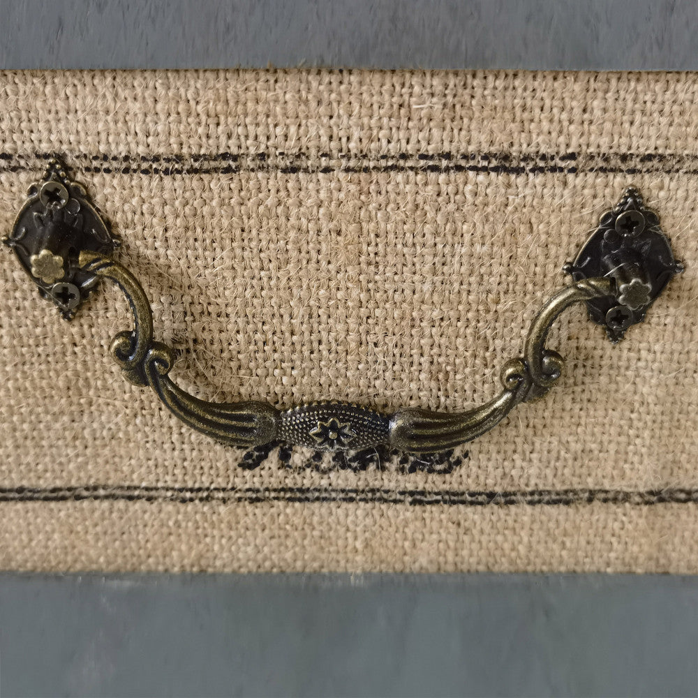 Primo piano della maniglia in metallo anticato e della texture ruvida in iuta sul cassetto centrale sfoderabile.