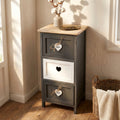 Mobiletto a tre cassetti in stile shabby chic grigio e bianco, posizionato in un angolo luminoso con un vaso di fiori di cotone sulla superficie in legno naturale.