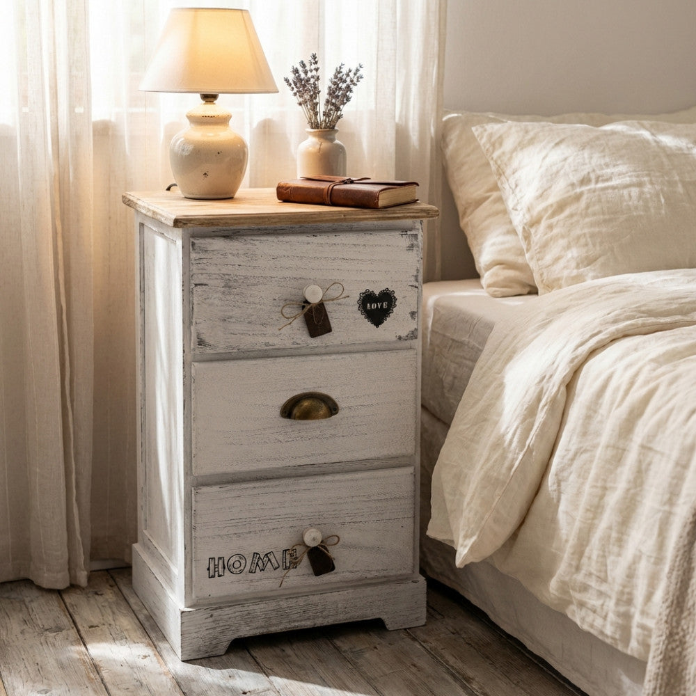 Comodino Ander in legno bianco shabby chic ambientato in una camera da letto luminosa.