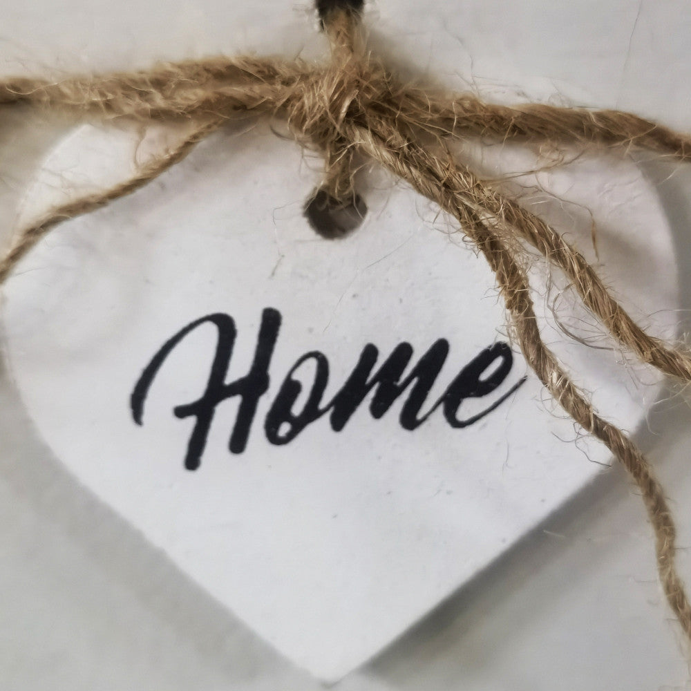 Dettaglio ravvicinato del pendente a forma di cuore con scritta Home e corda in iuta.