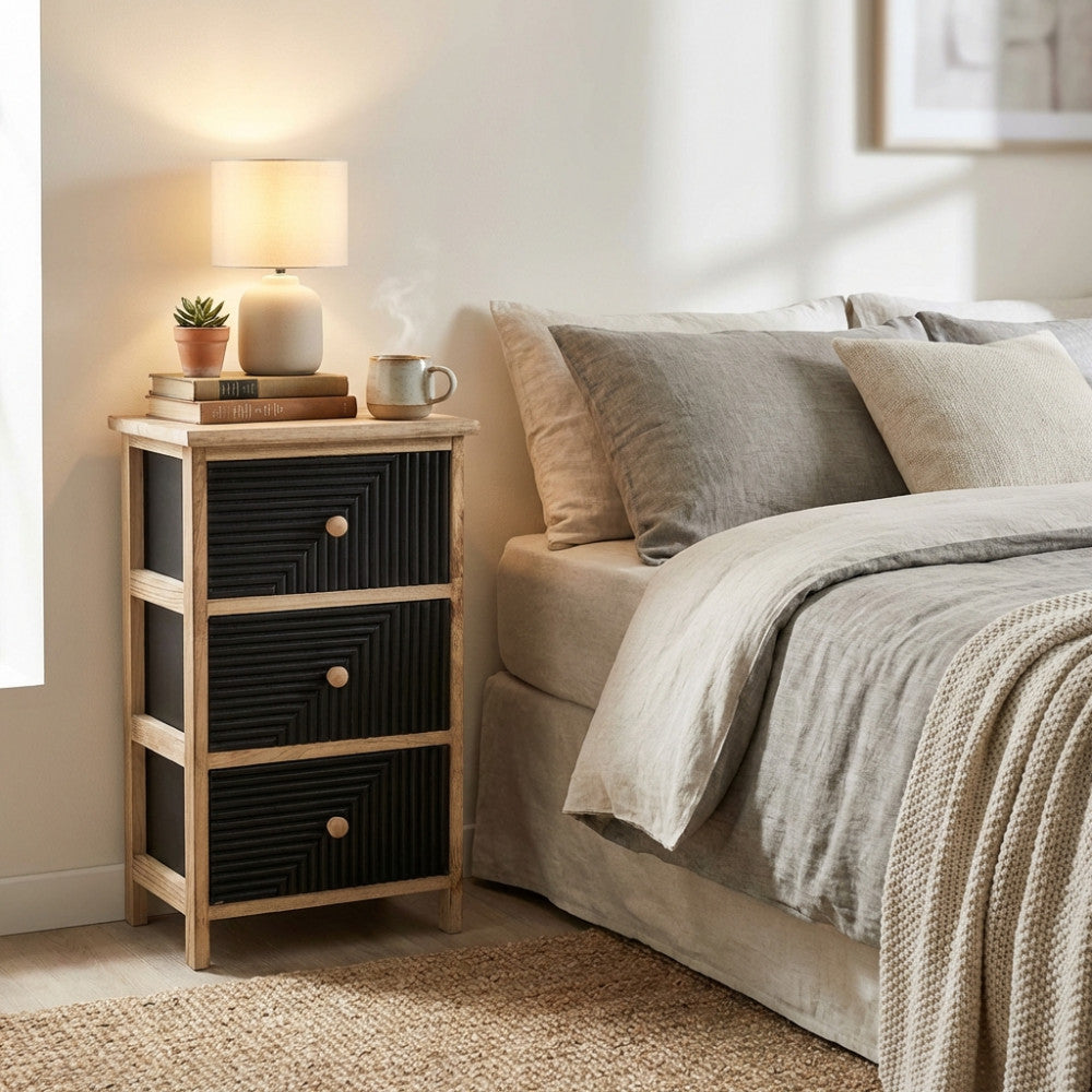 Vista angolare del comodino Anton utilizzato come tavolino da notte, decorato con una lampada in ceramica e una tazza fumante.