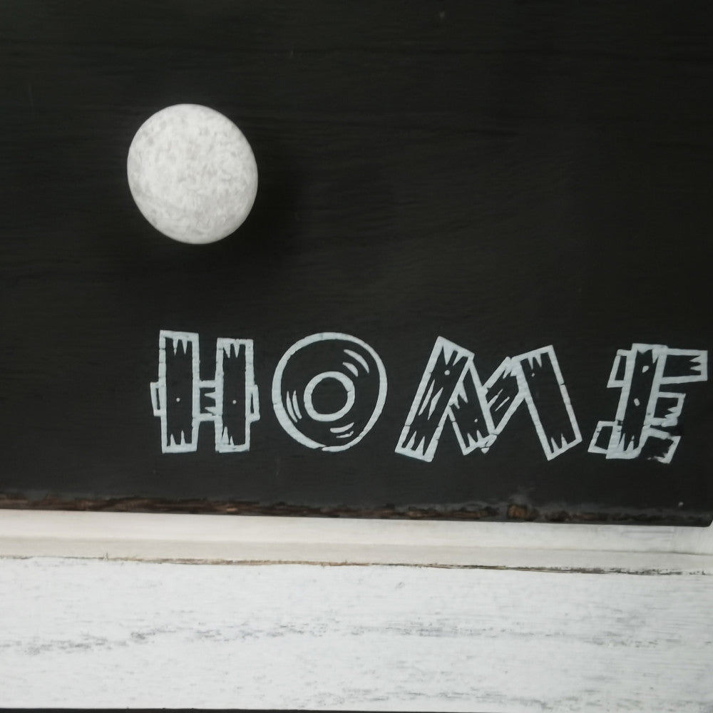 Primo piano del pomello bianco e della scritta decorativa HOME sul cassetto scuro.