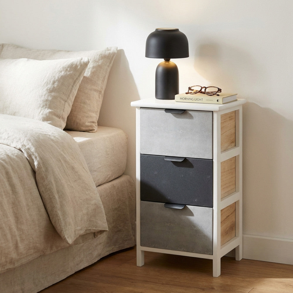 Comodino Casimiro utilizzato come tavolino da notte accanto a un letto in lino, illuminato da una lampada da tavolo nera.