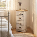 Mobiletto ANDER a 4 cassetti in legno decapé bianco, ambientato in una luminosa camera da letto shabby chic accanto a un letto in ferro battuto.