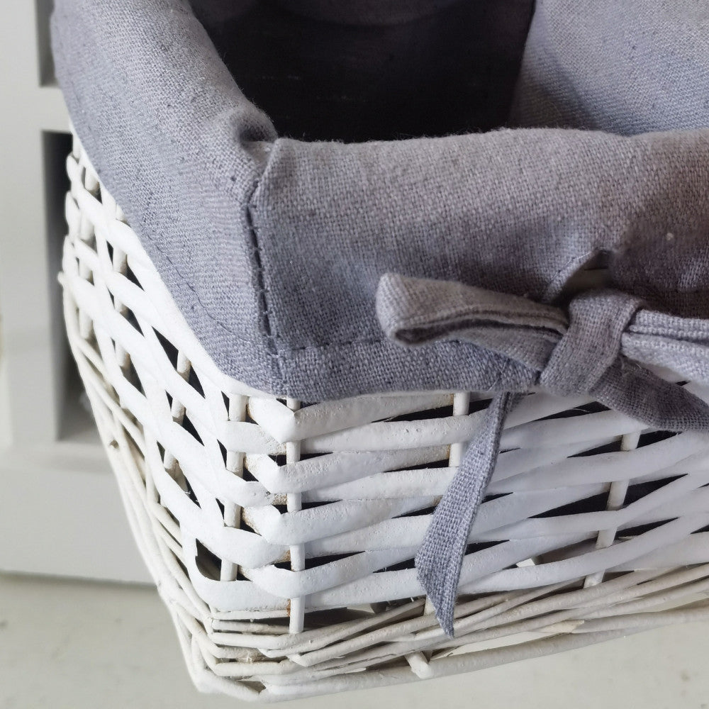Primo piano della cesta in vimini bianco con fodera in tessuto grigio e fiocco decorativo.