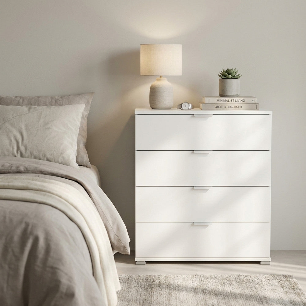 Cassettiera bianca a quattro cassetti in truciolare bilaminato, ambientata in una camera da letto moderna con lampada da tavolo.