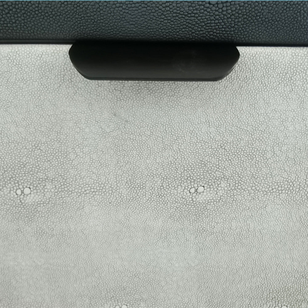 Dettaglio ravvicinato della texture effetto shagreen del cassetto grigio chiaro con maniglia in metallo nero.