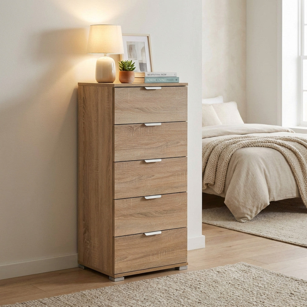 Vista angolare della cassettiera naturale posizionata accanto a un letto, decorata con una lampada da tavolo e libri.