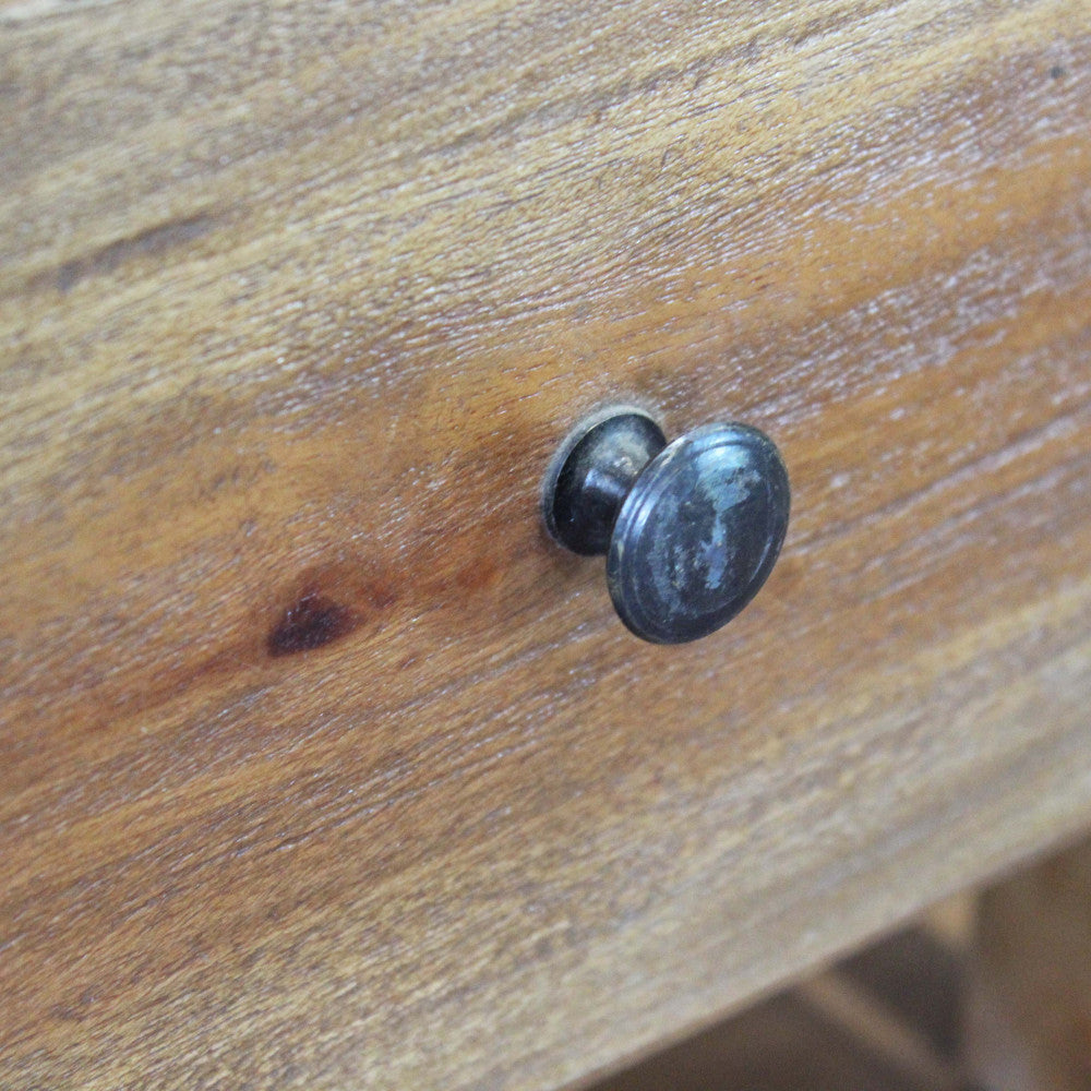 Dettaglio del pomello rotondo in metallo scuro dal fascino vintage sul cassetto in legno.