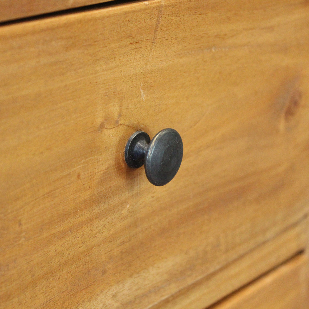 Primo piano del pomello rotondo in metallo scuro, applicato sul frontale in legno marrone del cassetto.
