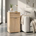 Comodino MR805044 in truciolare bilaminato marrone chiaro, ambientato accanto a un divano grigio con lampada di design.