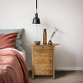 Mobiletto Farran in pino riciclato utilizzato come comodino accanto a un letto con biancheria color ruggine.