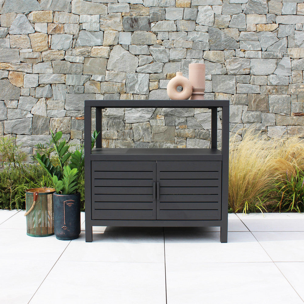 Mobiletto Phoenix inserito in un contesto outdoor con muro in pietra e piante decorative.