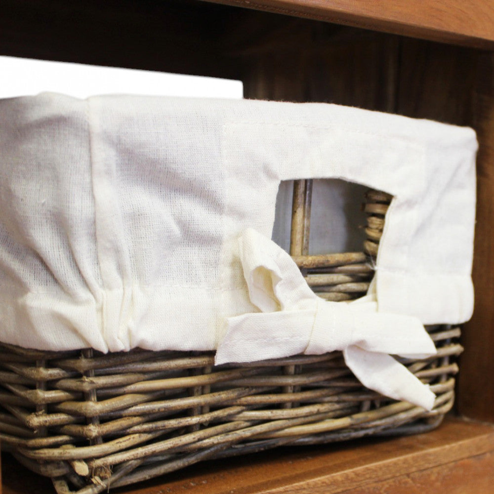 Dettaglio ravvicinato del cesto in rattan intrecciato con rivestimento in cotone bianco sfoderabile e fiocco decorativo.