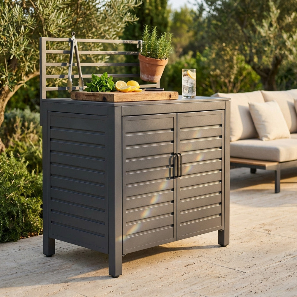 Modulo cucina da esterno Oklahoma in alluminio antracite, allestito con tagliere in legno, limoni freschi e piante aromatiche in un rigoglioso giardino.