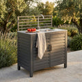 Modulo con lavello per cucina da esterno Oklahoma in alluminio antracite, ambientato in un giardino rigoglioso con luce dorata del tramonto.