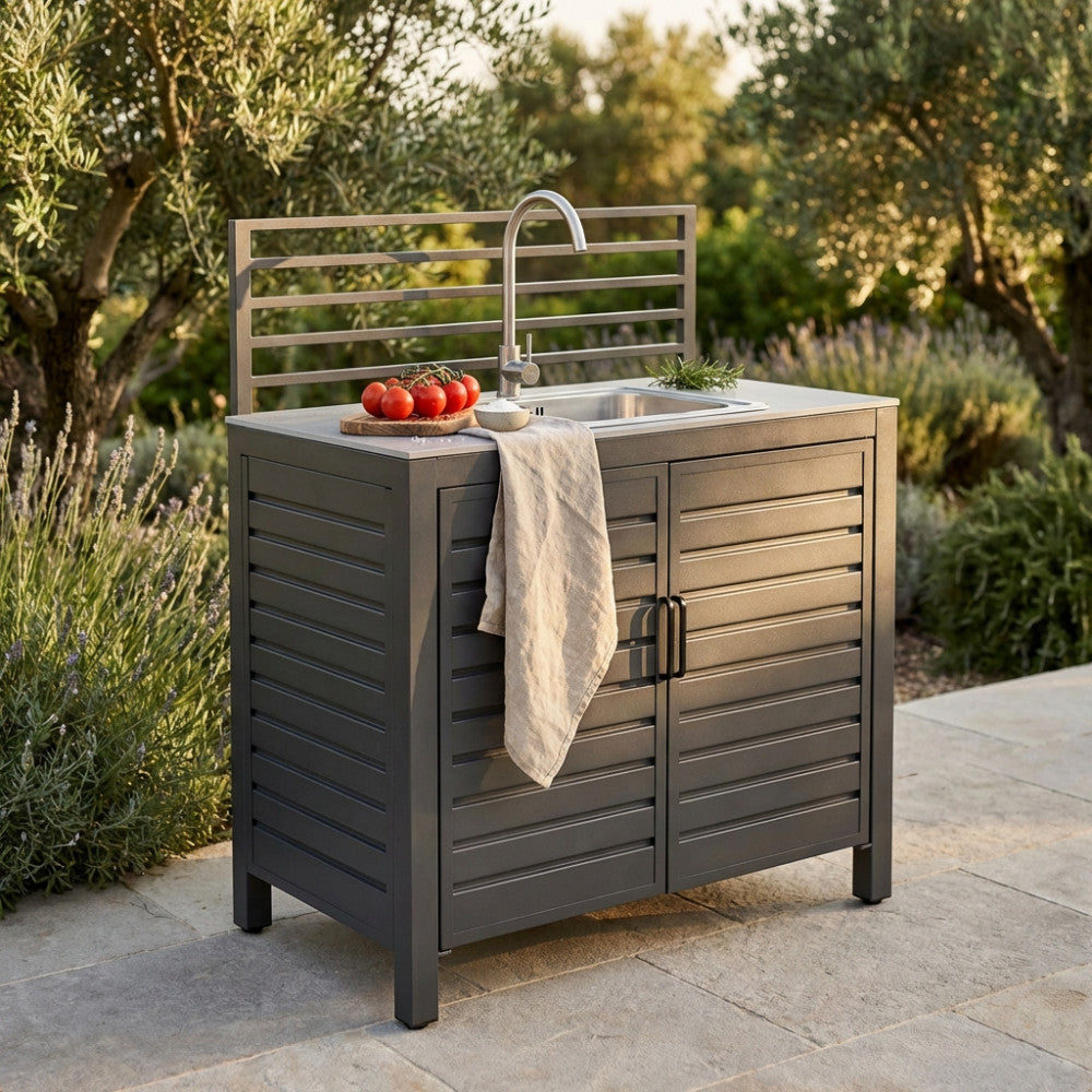 Modulo con lavello per cucina da esterno Oklahoma in alluminio antracite, ambientato in un giardino rigoglioso con luce dorata del tramonto.