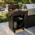 Modulo cucina esterna in metallo nero con tagliere e verdure, affiancato a un barbecue a gas in acciaio.