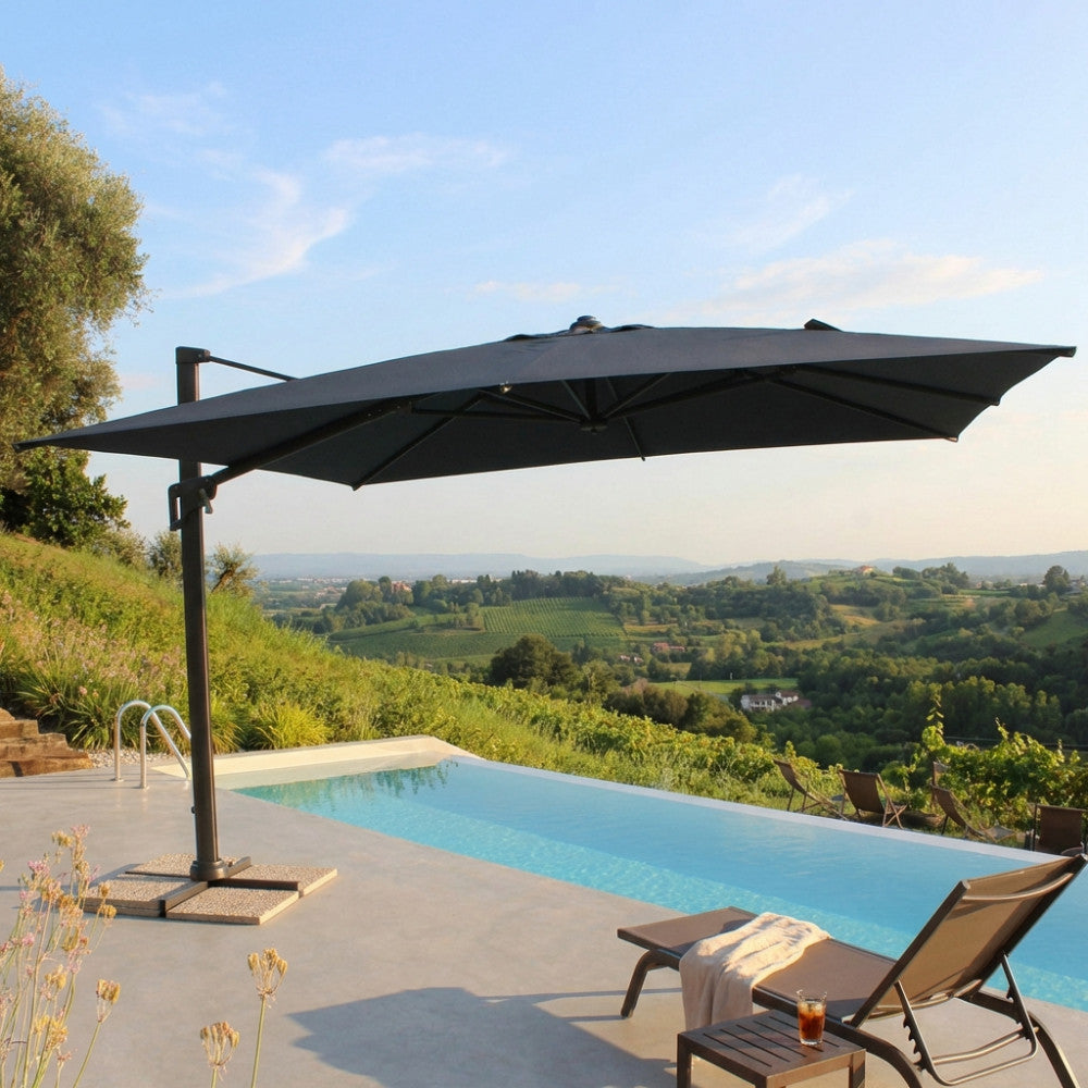 Vista laterale dell'ombrellone Acrux 4x4 che proietta un'ampia ombra su lettini prendisole eleganti in un giardino di lusso.