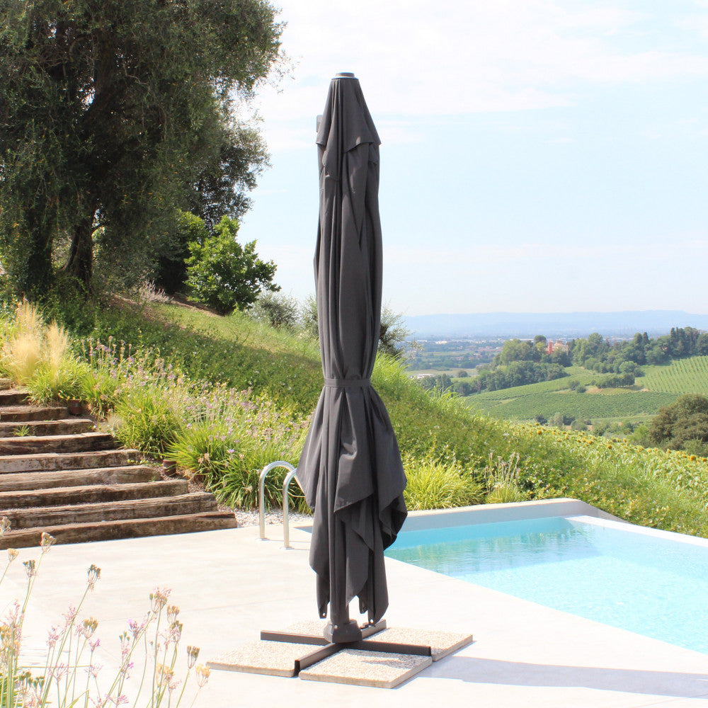 Ombrellone Acrux chiuso a bordo piscina, con il telo in poliestere grigio scuro elegantemente ripiegato lungo il palo in alluminio.