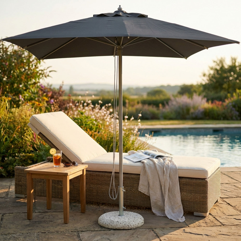 Dettaglio dell'ombrellone Andromeda in alluminio e poliestere grigio, posizionato accanto a un lettino in rattan sintetico a bordo piscina.