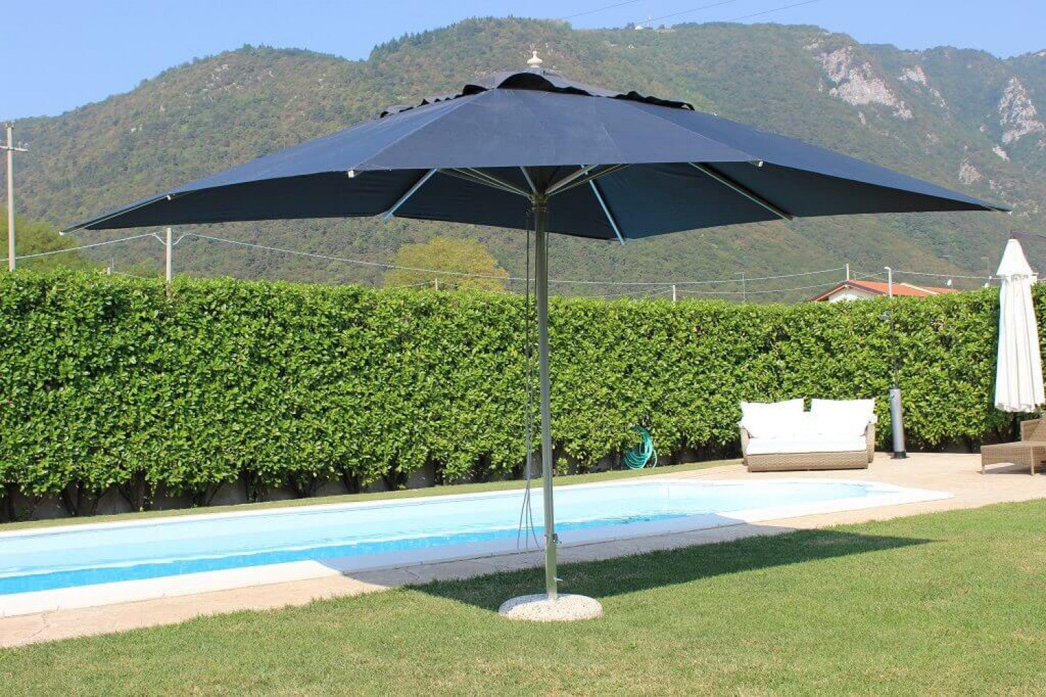 Ombrellone Andromeda grigio aperto in un ampio giardino verde con piscina, mostrando la sua capacità di ombreggiare grandi spazi esterni.
