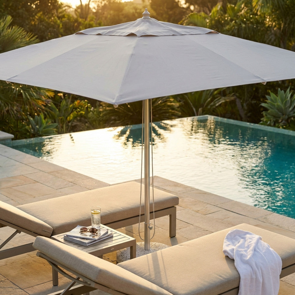 Vista ravvicinata dell'ombrellone a palo centrale Andromeda che proietta un'ombra elegante su lettini outdoor di design.