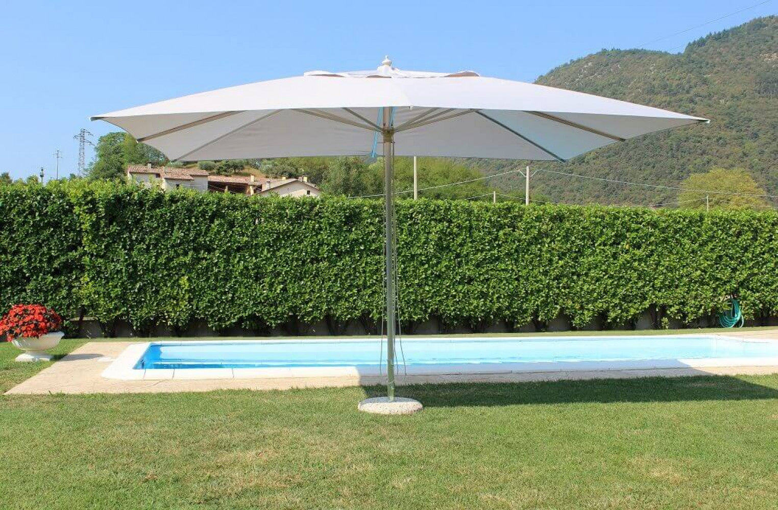Ombrellone Andromeda posizionato su un prato verde curato vicino a una piscina, evidenziando la sua ampia zona d'ombra.
