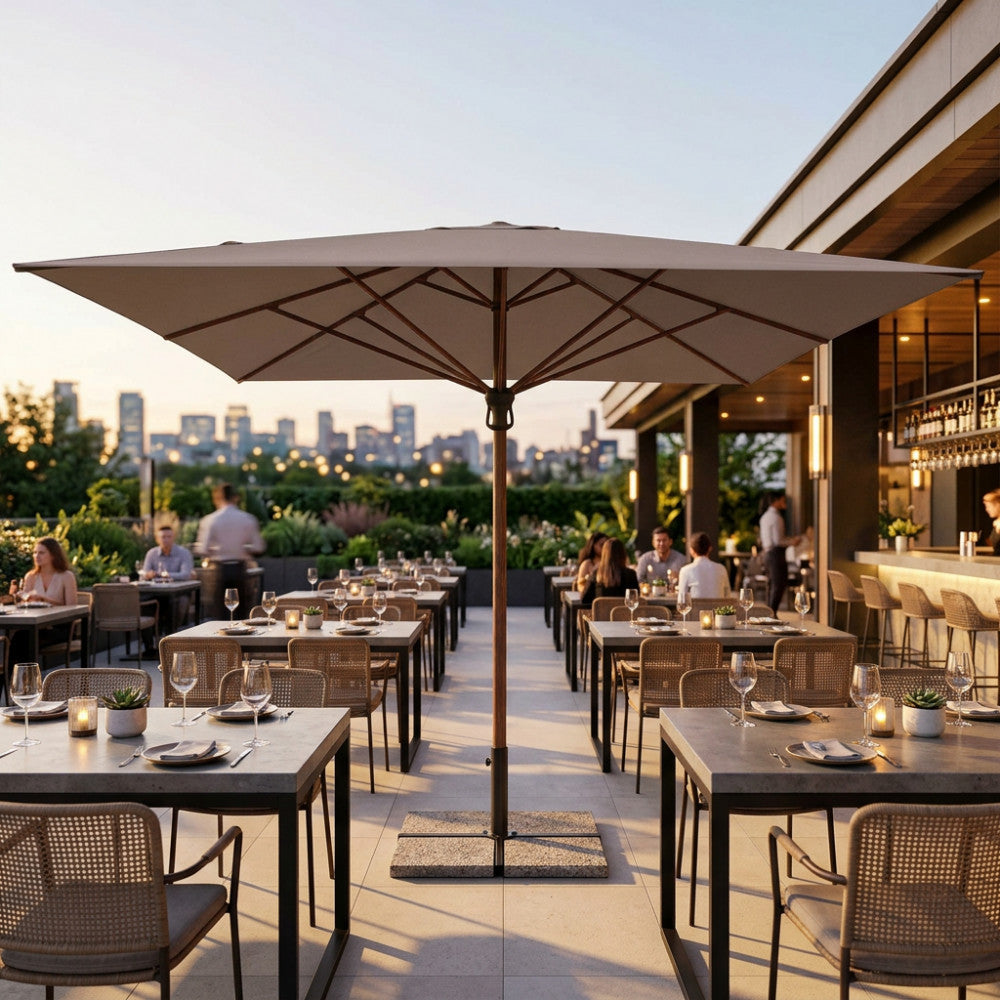 Dettaglio dell'ombrellone Arneb con copertura in poliestere taupe, che ombreggia una sofisticata terrazza lounge al tramonto con vista panoramica.