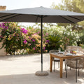 Ombrellone Brian aperto in un giardino lussuoso, con telo grigio e palo centrale nero in alluminio.