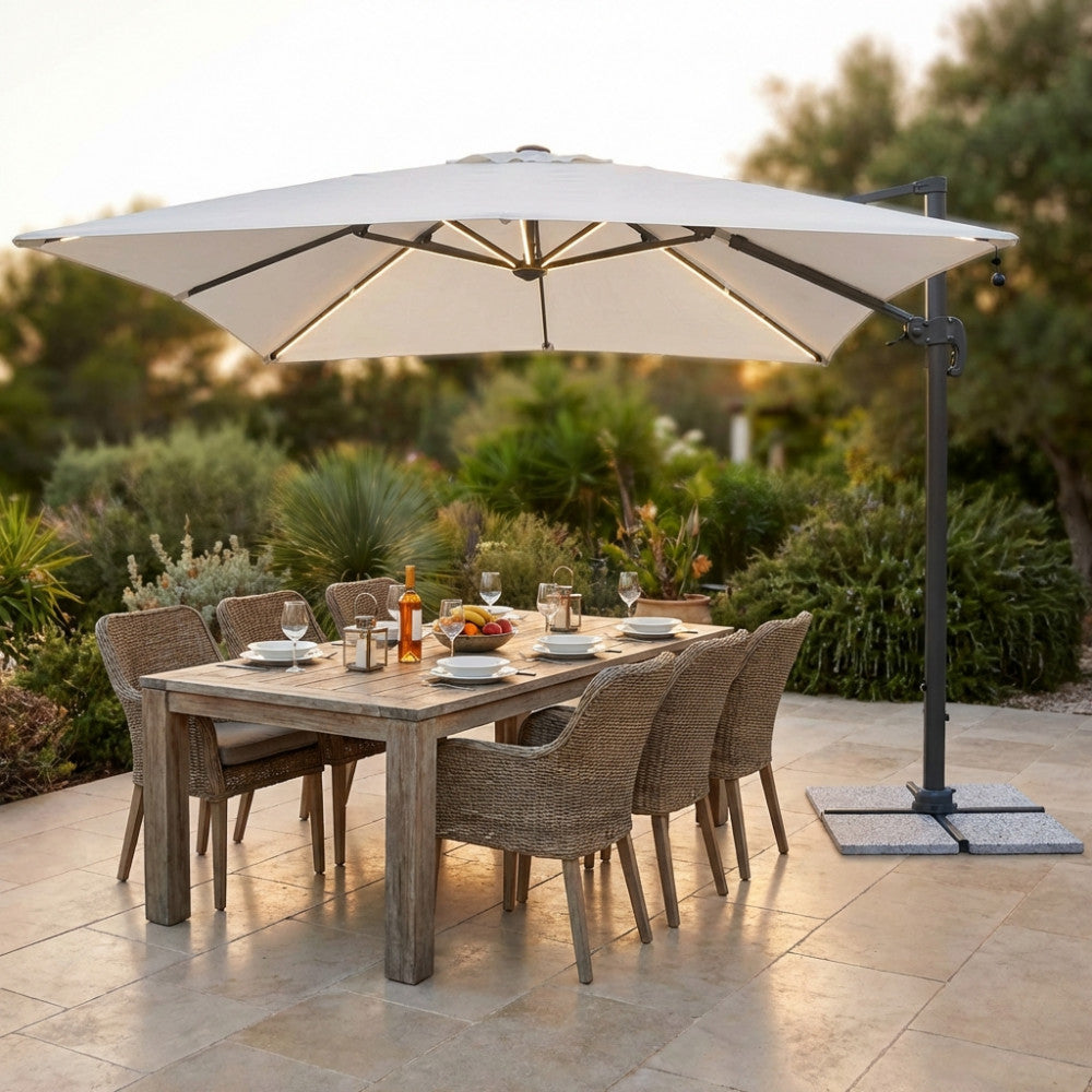 Dettaglio dell'ombrellone Pitagora in alluminio antracite che illumina un set da pranzo in rattan intrecciato durante il tramonto.