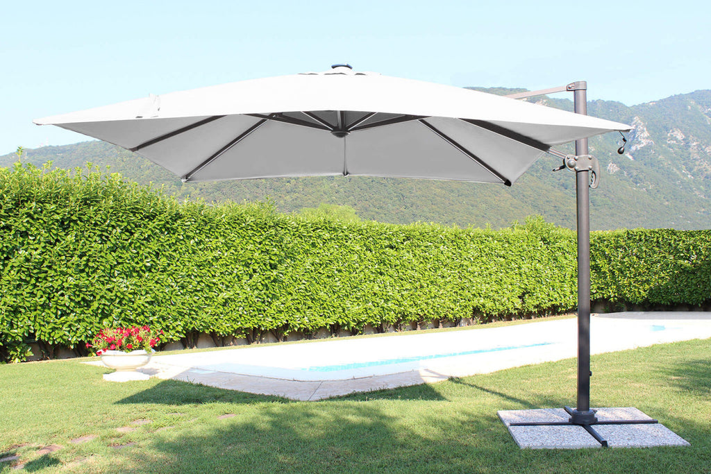 Ombrellone a palo laterale Pitagora aperto di giorno, con telo in poliestere grigio, a bordo di una piscina circondata dal verde.