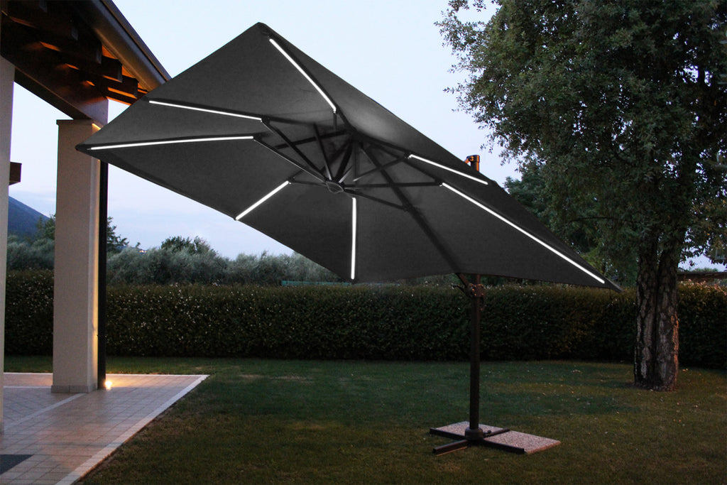 Atmosfera notturna con l'ombrellone Pitagora illuminato dai LED integrati sulle stecche, che crea un ambiente suggestivo in giardino.