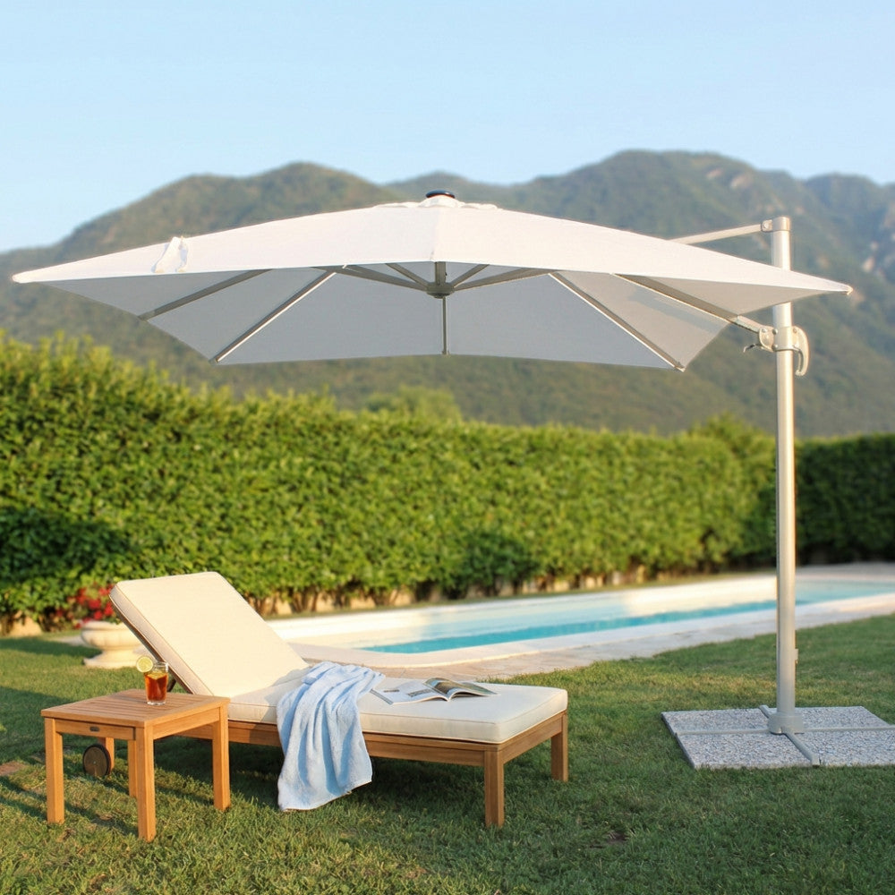 Ombrellone in alluminio e poliestere bianco che fa ombra a un lettino prendisole in teak vicino alla piscina.