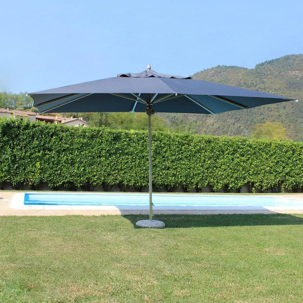Ombrellone a palo centrale aperto su un prato curato vicino a una piscina, evidenziando l'ampia zona d'ombra generata.