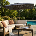 Ombrellone Cristal 3x4 grigio aperto su un salotto da esterni con divano beige e piscina.