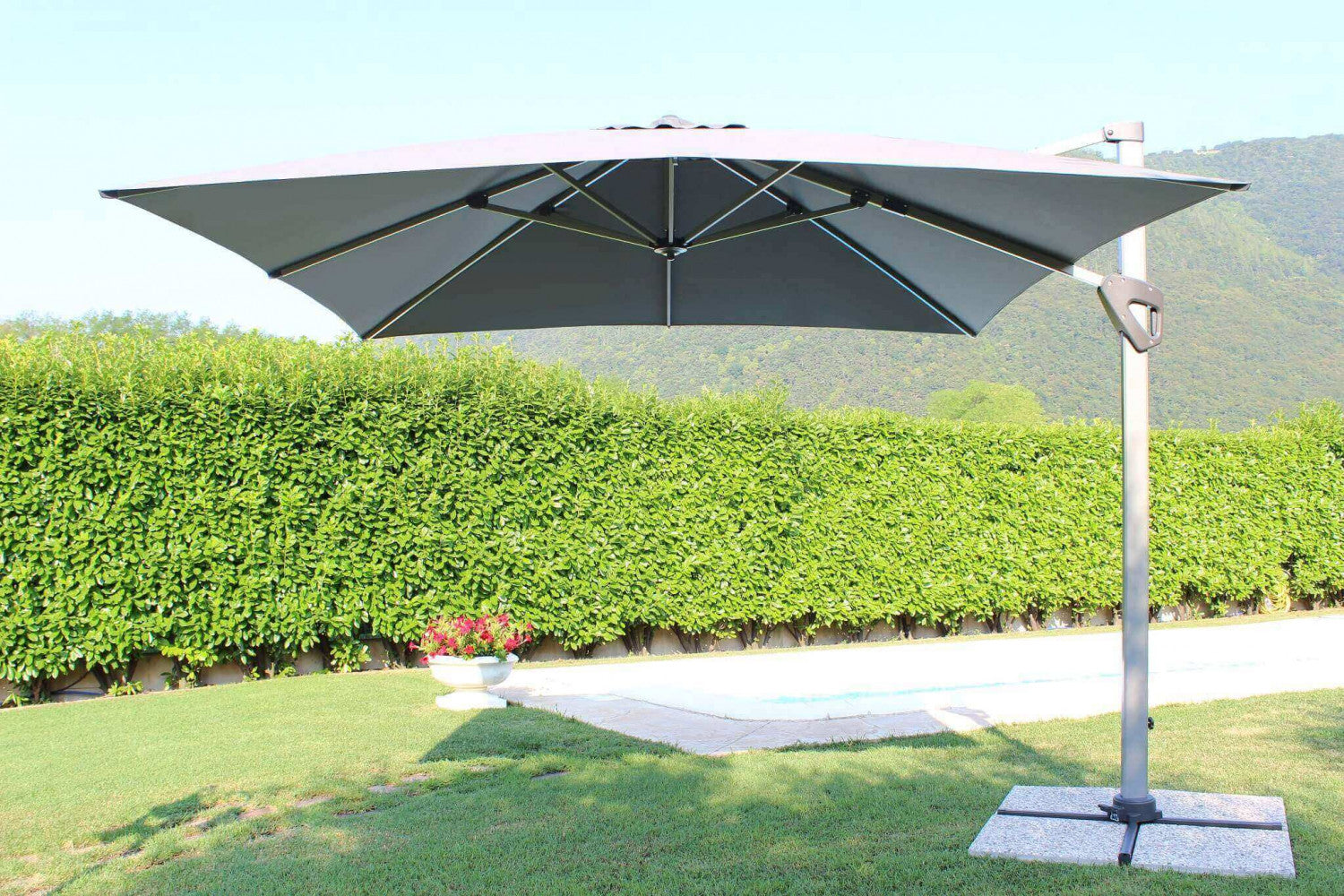 Ombrellone da giardino grigio posizionato su un prato verde vicino a una siepe.