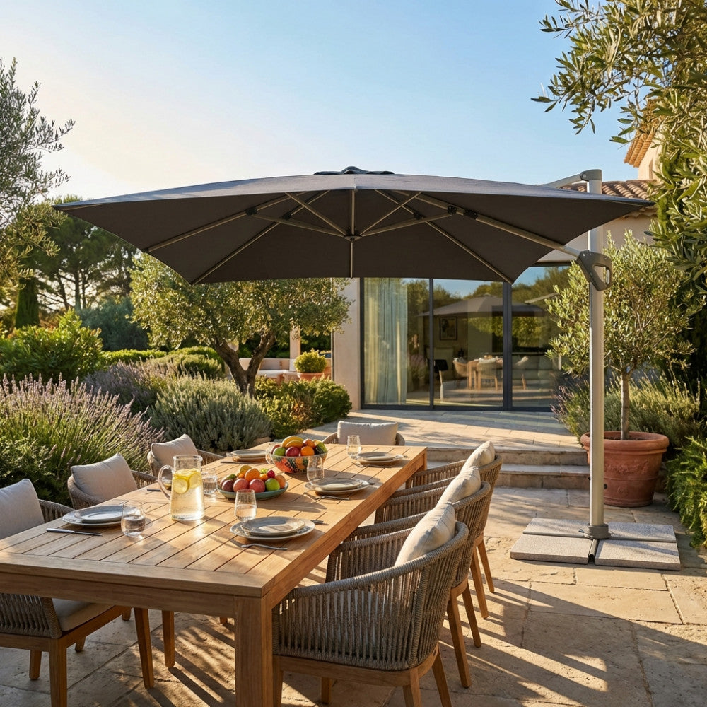 Ombrellone Darwin grigio 3x4 aperto su un tavolo da pranzo in legno in un giardino lussuoso.
