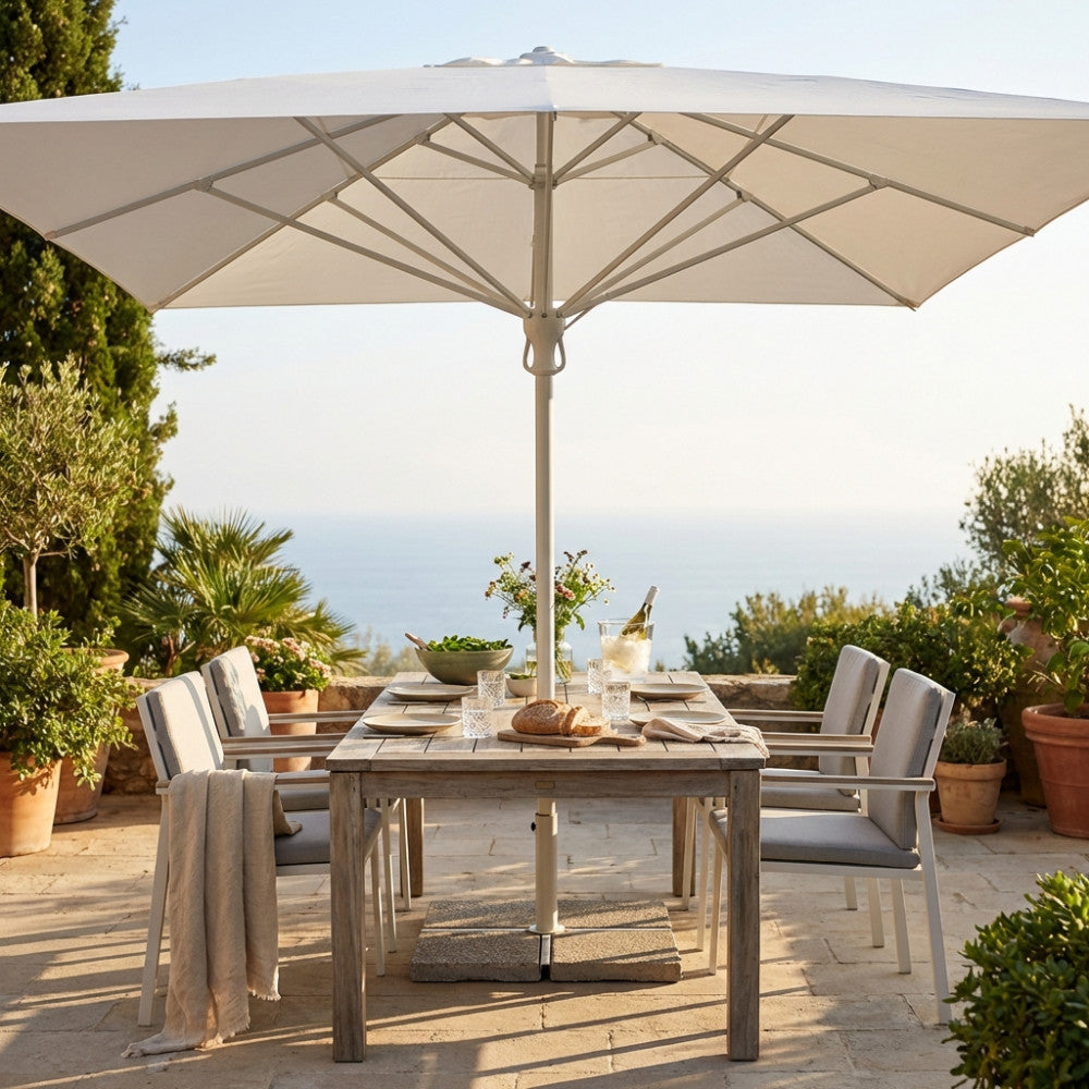Ombrellone a palo centrale bianco aperto su un tavolo da pranzo in legno in una terrazza vista mare.