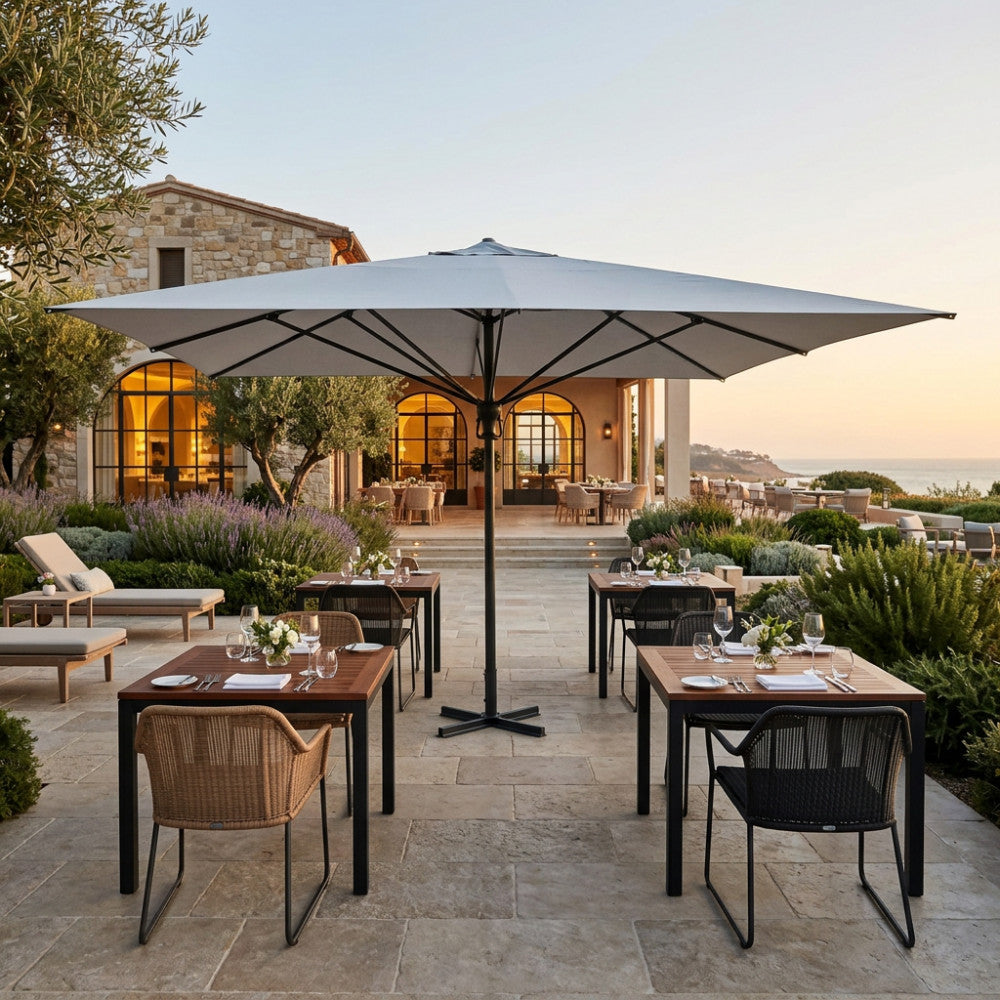 Ombrellone moderno Deneb 5x5 metri che ombreggia un'elegante area dining esterna al tramonto.