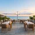Ombrellone doppio Archimede bianco posizionato su una terrazza ristorante vista mare al tramonto.
