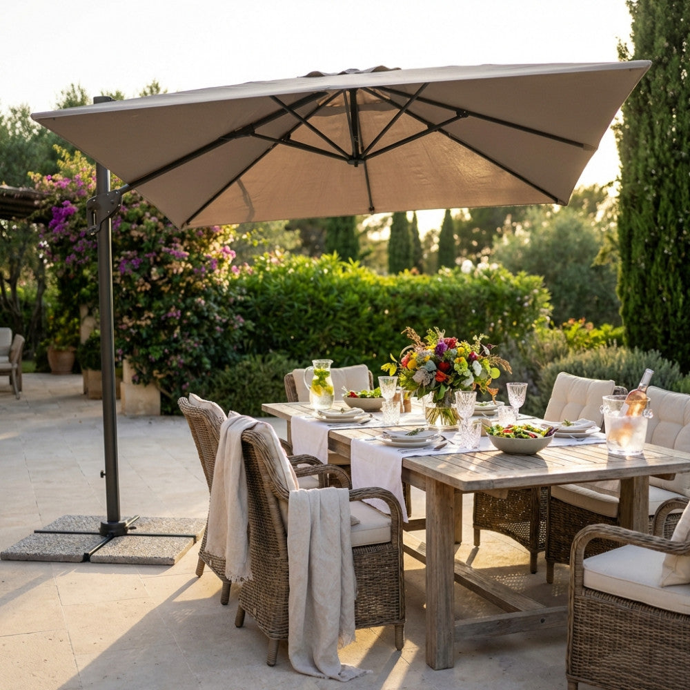 Ombrellone Garnet con telo taupe che ombreggia un elegante tavolo da pranzo in legno in un giardino rigoglioso.