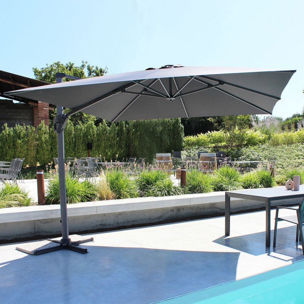 Ombrellone Mendel aperto a bordo piscina, che proietta un'ampia ombra su un'area lounge esterna.