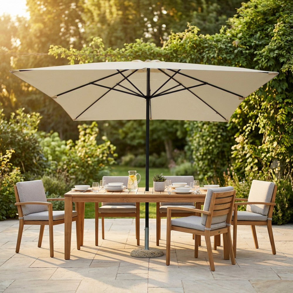 Vista frontale dell'ombrellone Mercurio con telo ecrù che ombreggia un set da pranzo in teak in un giardino rigoglioso.