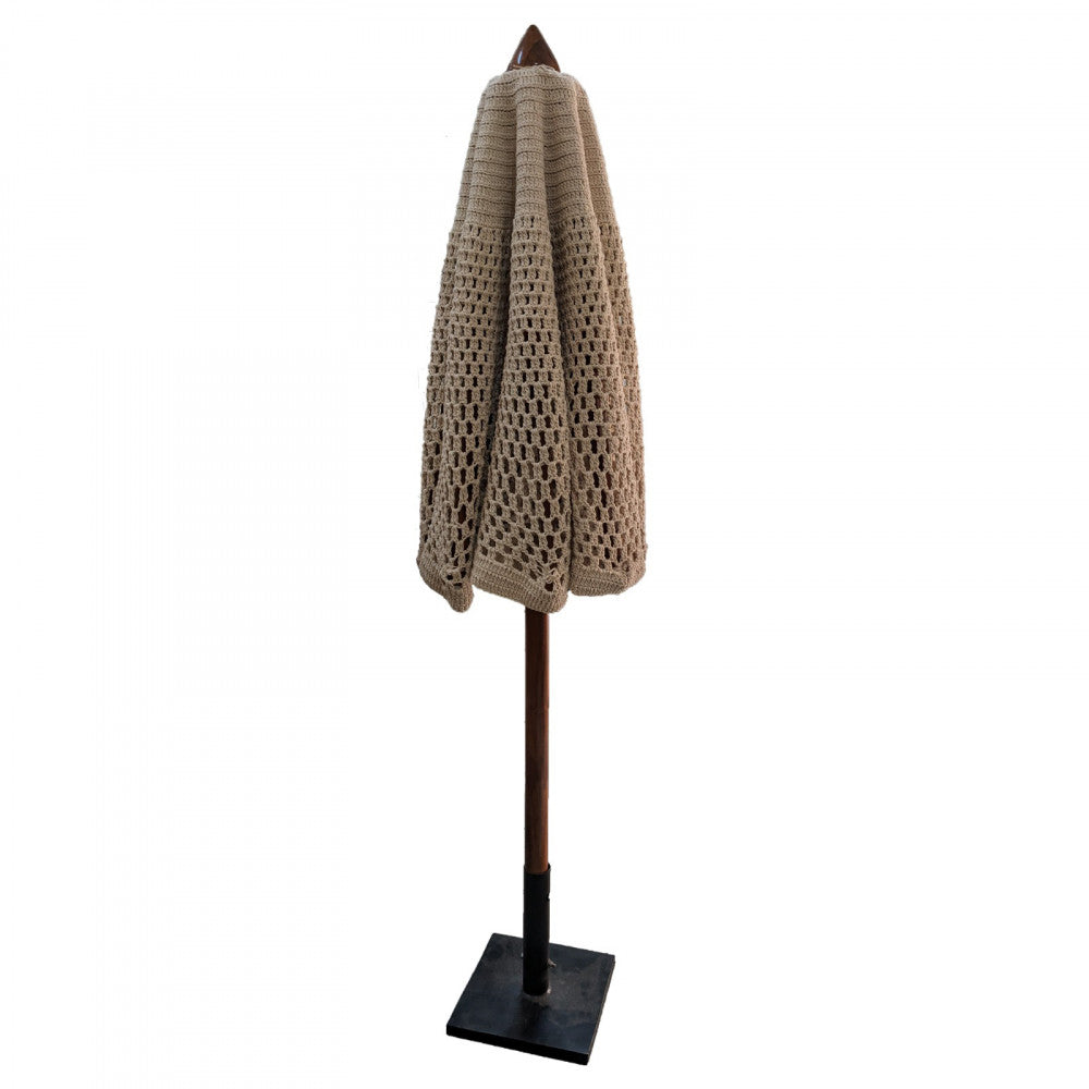 Ombrellone Nador chiuso, con la copertura in cotone beige ripiegata lungo il palo centrale in acacia, supportato dalla base quadrata in metallo.
