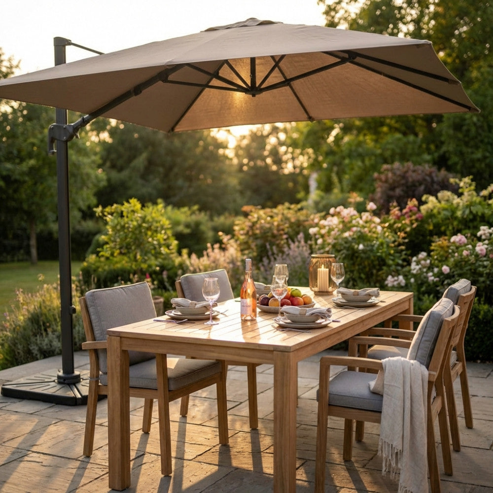 Ombrellone a braccio 3x4 aperto su un tavolo da pranzo in legno di teak in un rigoglioso giardino al tramonto.