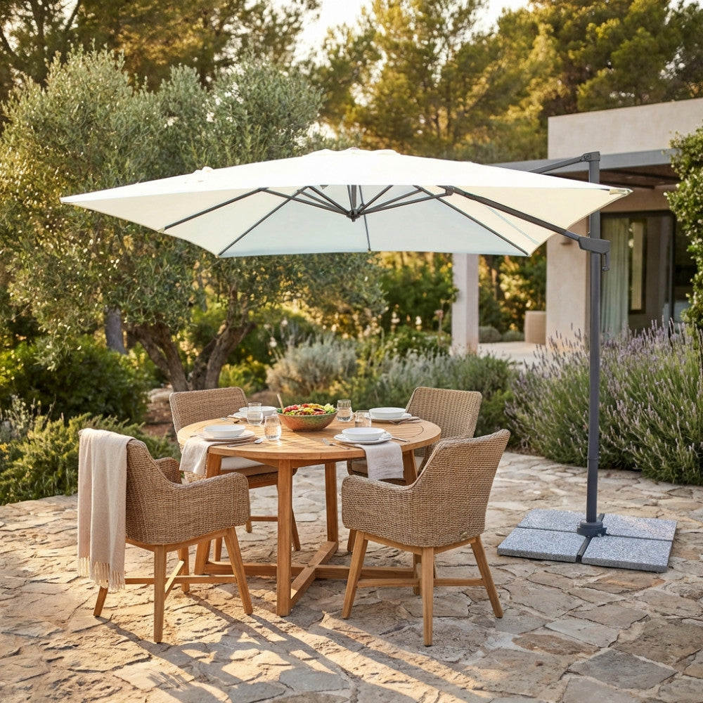 Ombrellone Newton in alluminio nero che ombreggia un tavolo da pranzo in teak con sedie in rattan in un giardino.