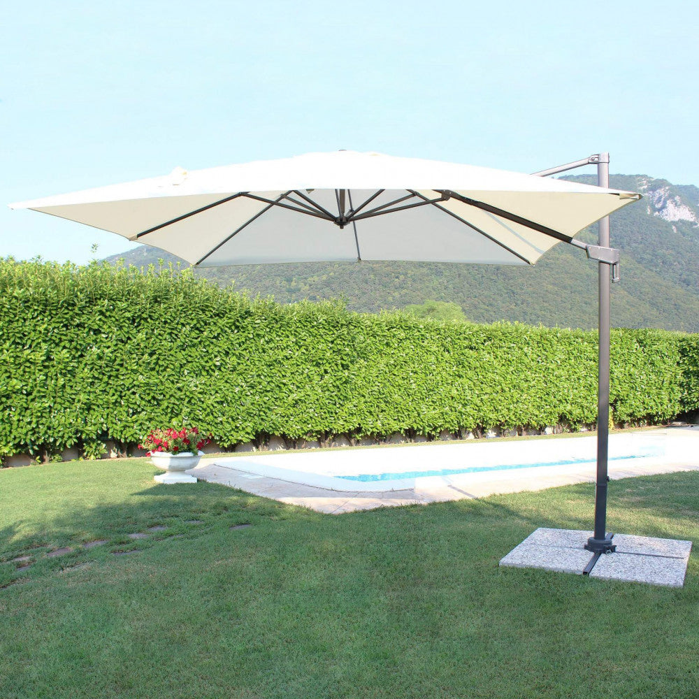 Ombrellone Newton aperto a bordo piscina, con il telo ecrù che contrasta con il verde della siepe circostante.