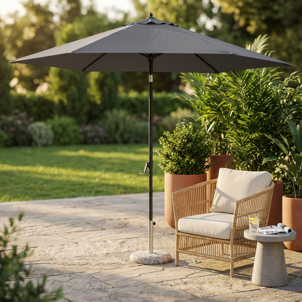 Ombrellone da giardino Nice con telo grigio scuro e palo centrale nero, ambientato accanto a una poltrona in midollino.