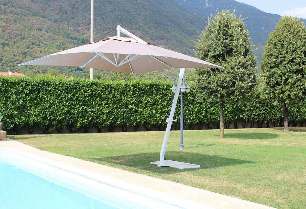 Ombrellone Pegaso aperto a bordo piscina durante il giorno, che proietta un'ampia zona d'ombra sul prato.